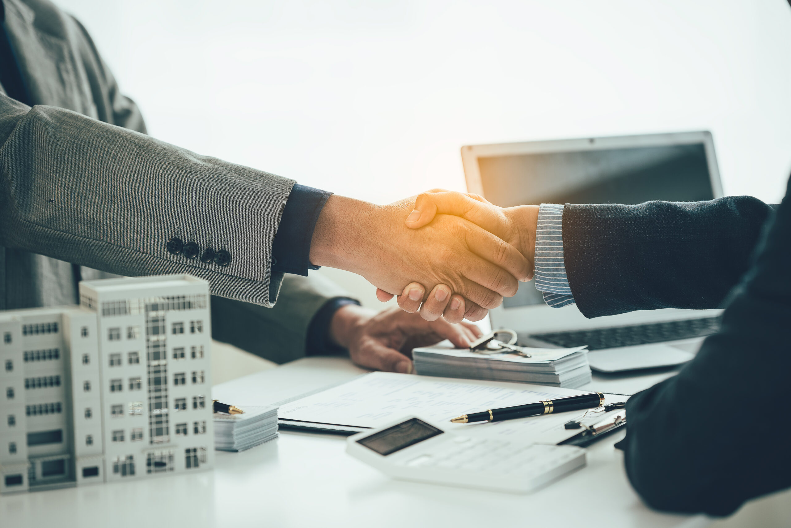 Handshake between professionals at Title Town Closing Group, with white desk, small architectural models, documents, and a laptop, reflecting comprehensive title services context